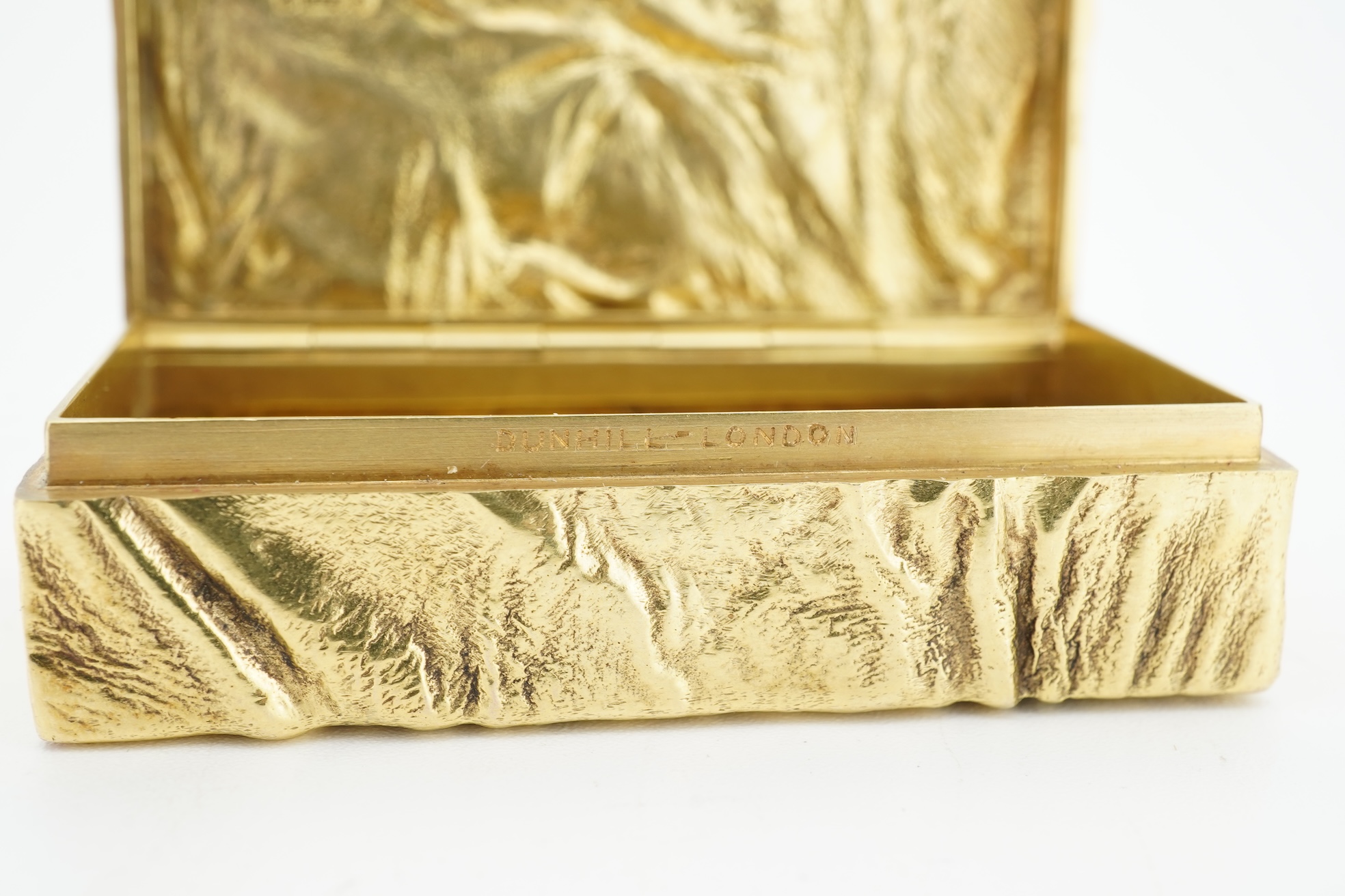 Dunhill, an attractive 9ct gold and sapphire snuffbox, circa 1973, the rectangular box of samorodok finish, the hinged lid set with a foil-backed oval sapphire, measuring approximately 5.1 x 2.7 x 1.6cm, signed Dunhill L